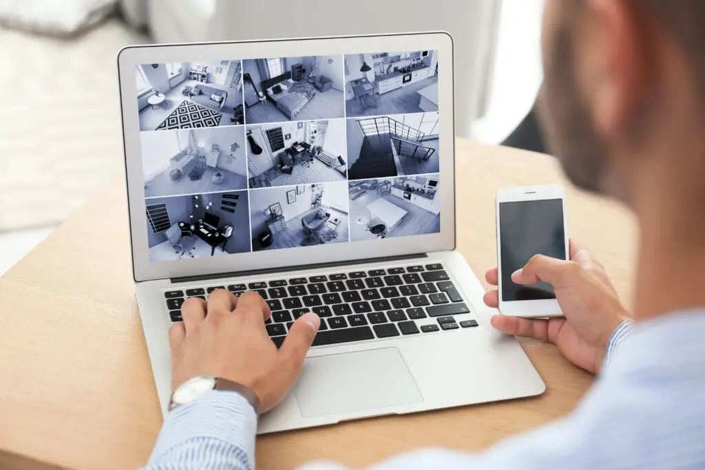 Person monitoring multiple live CCTV security camera feeds on a laptop.